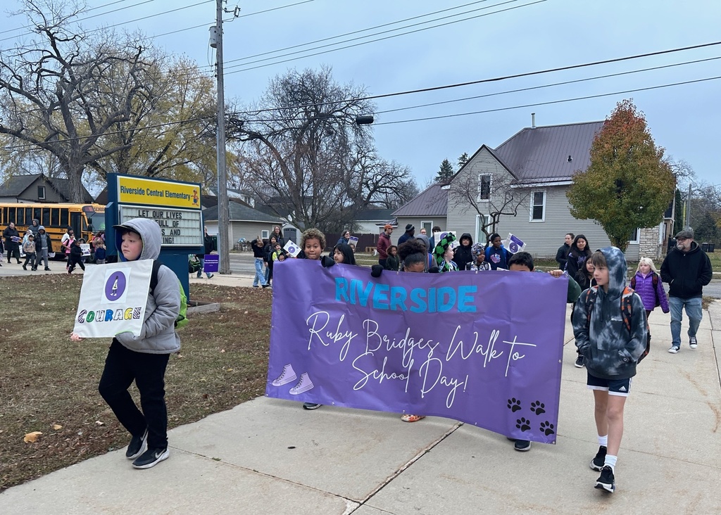 Students and families walking behind a purple banner