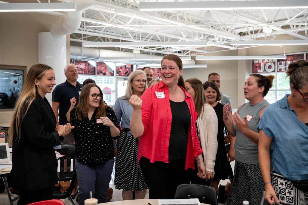 Group of new teachers smile and cheer for the winner of rock paper scissors.