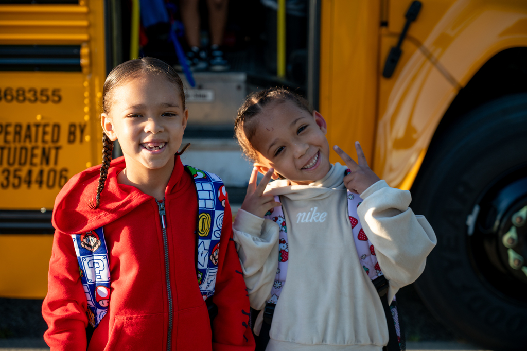 Two students smiling at the camera outside the bus