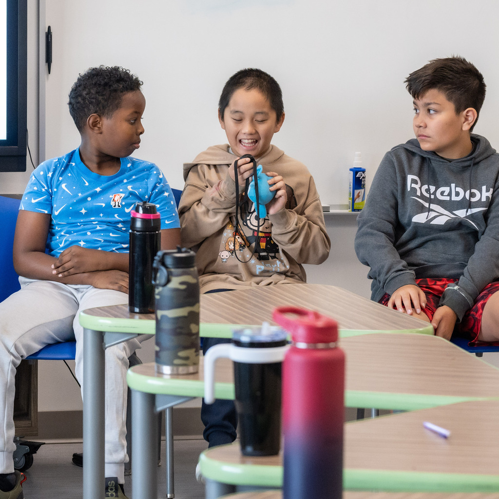 Two students listen to their classmate speak gleefully into the microphone.