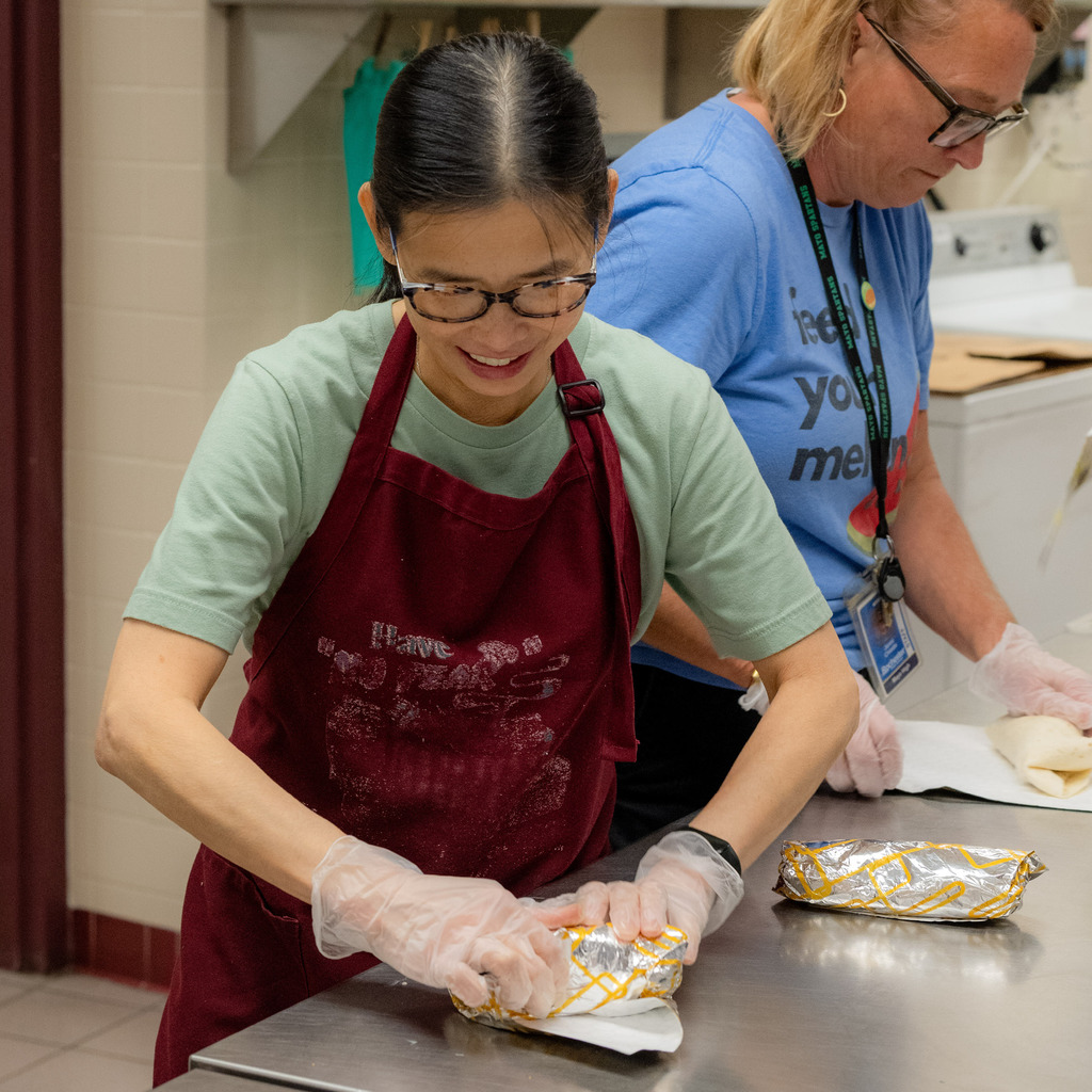 Student Nutrition Services employee rolls a wrap together in tin foil.