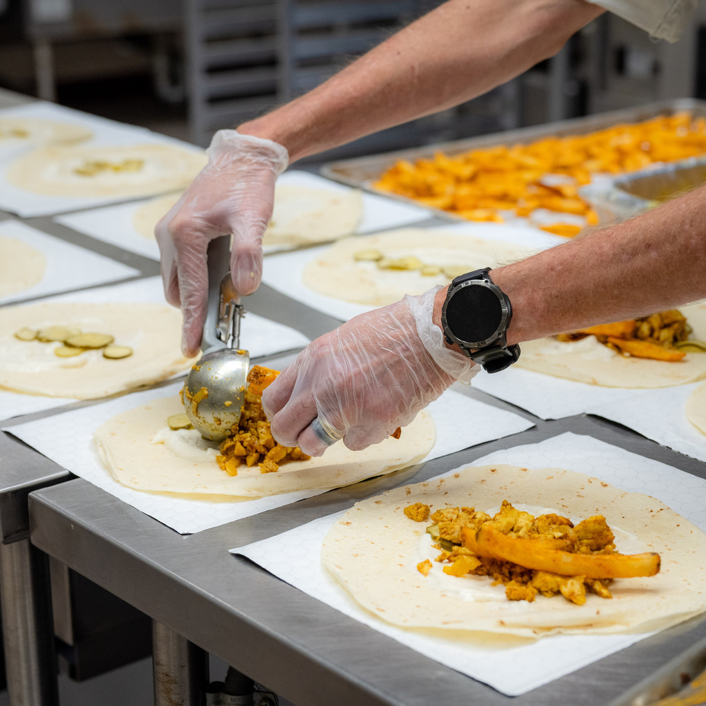 Gloved hands assemble a Chicken Shawarma Wrap.
