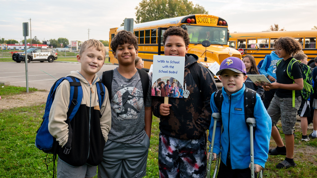Four boys pose for camera. One holds a sign reading, "walk to school with the school board."