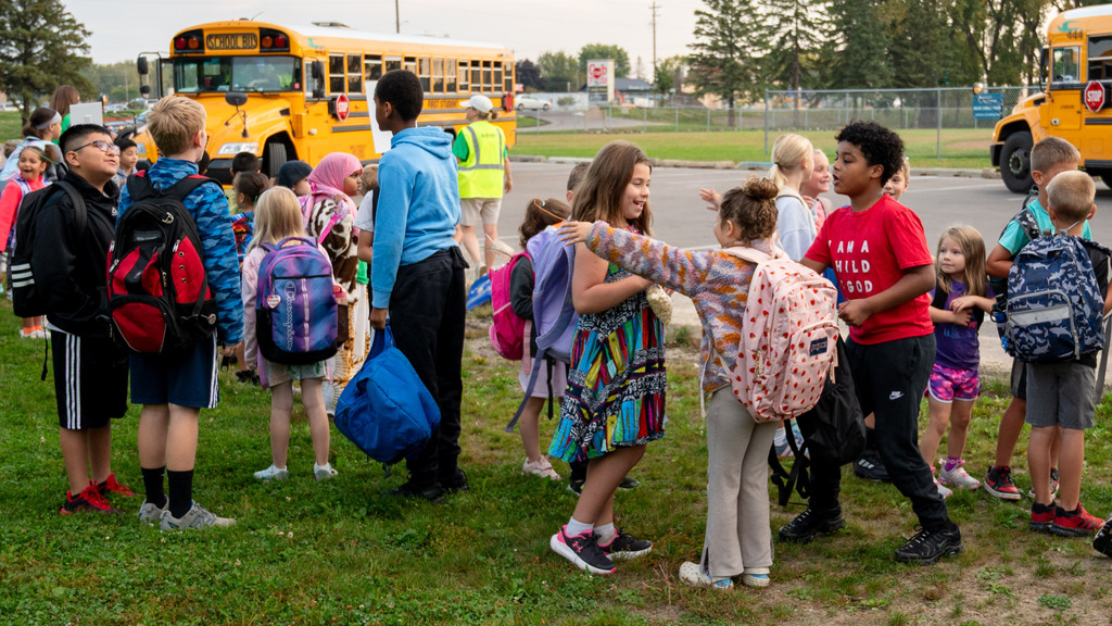 Kids chat with their friends after getting off school buses.