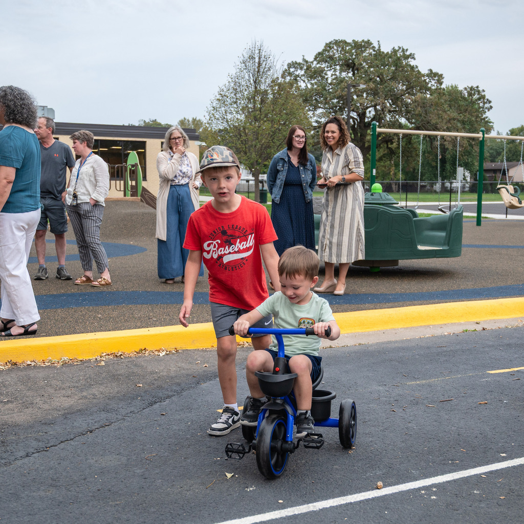 One brother helps another ride a scooter at the traffic garden.
