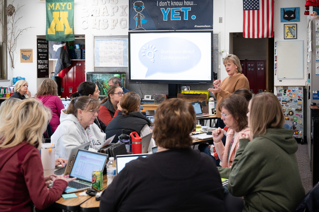 Folwell teachers and staff sit around tables and listen to Principal Kristin Smith's presentation. 