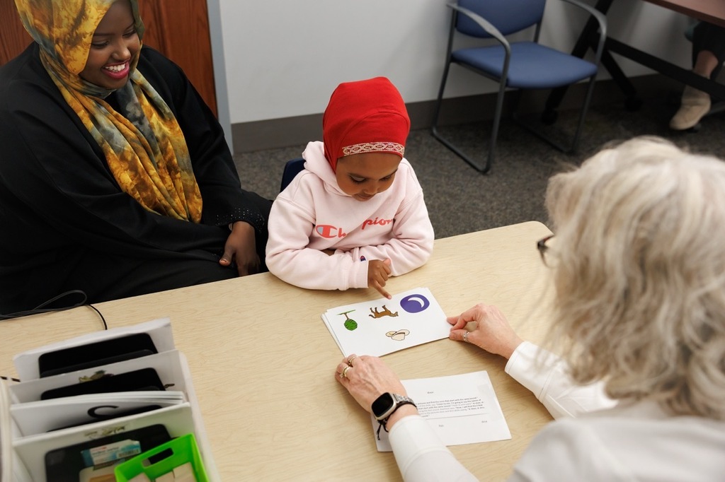 Parent smiling over student as they look at the screen cards presented by the teacher on the table.