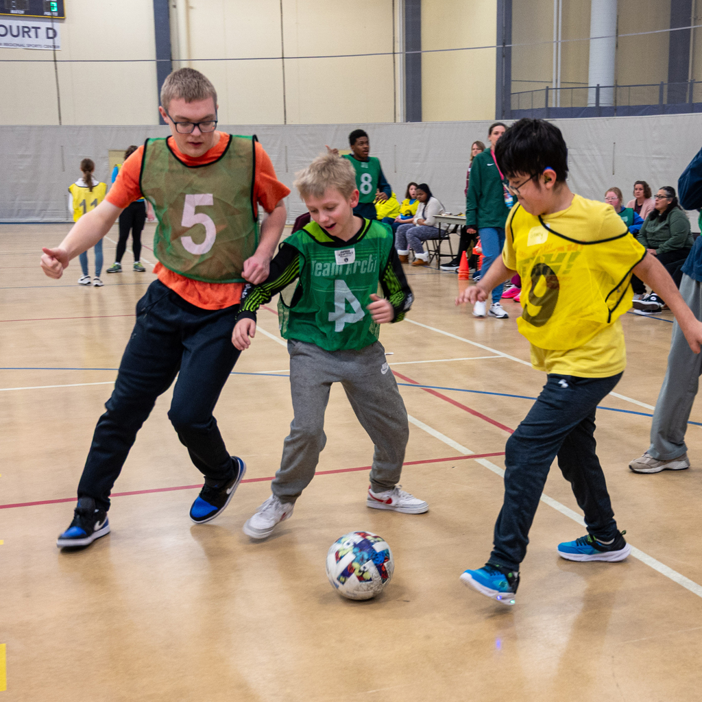 Students in green and yellow jerseys compete for a soccer ball.