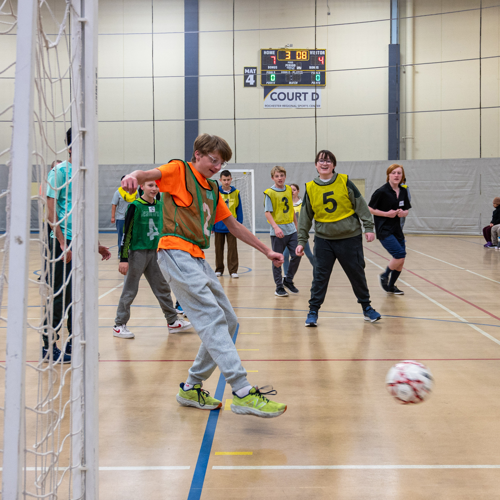 Students in green and yellow jerseys play soccer in a gym.
