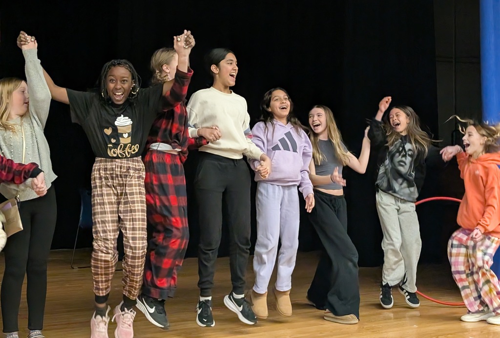 Students and staff wearing colorful clothing cheer and smile enthusiastically during a school competition, celebrating wins together in a lively, joyful atmosphere.