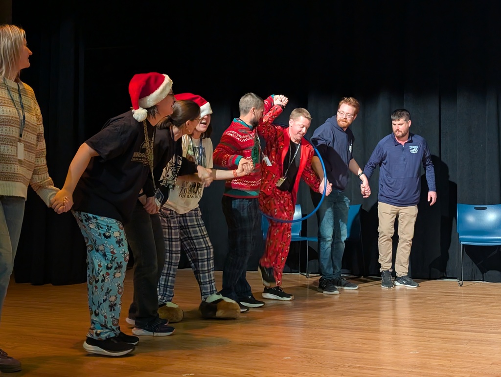 Students and staff wearing colorful clothing cheer and smile enthusiastically during a school competition, celebrating wins together in a lively, joyful atmosphere.
