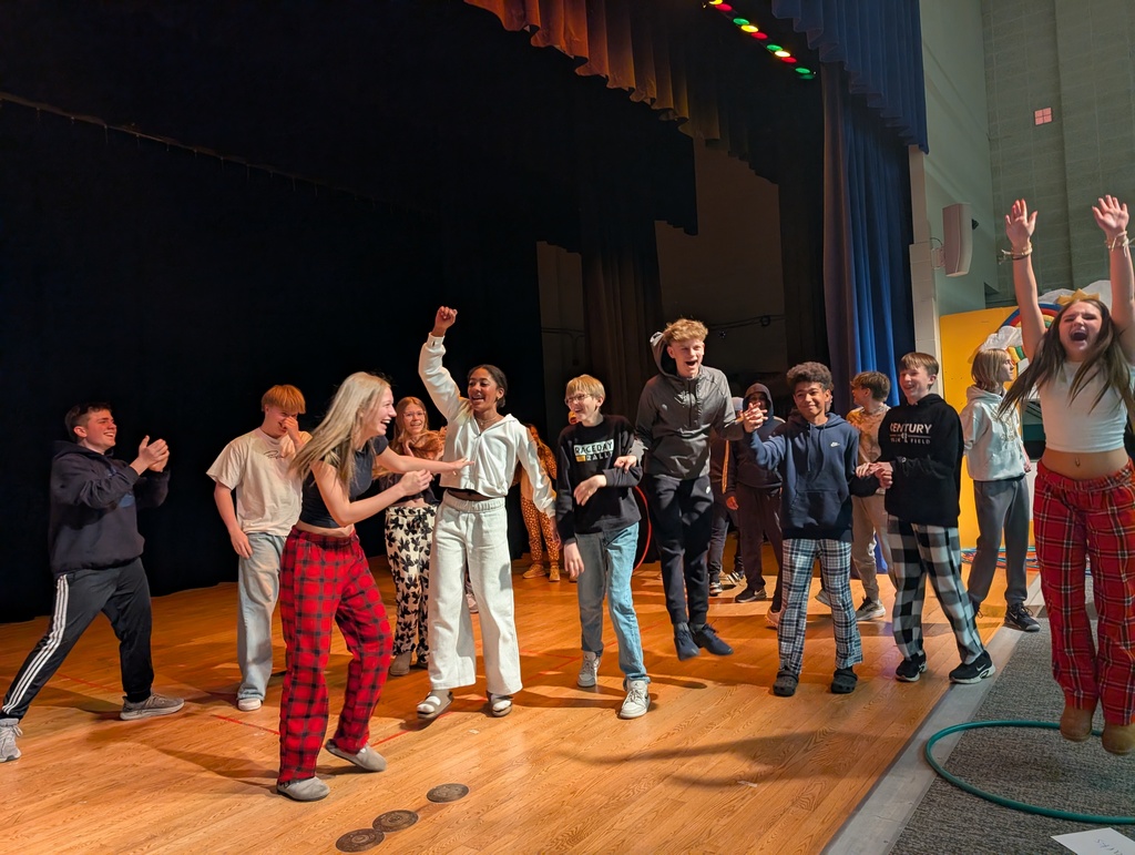 Students and staff wearing colorful clothing cheer and smile enthusiastically during a school competition, celebrating wins together in a lively, joyful atmosphere.