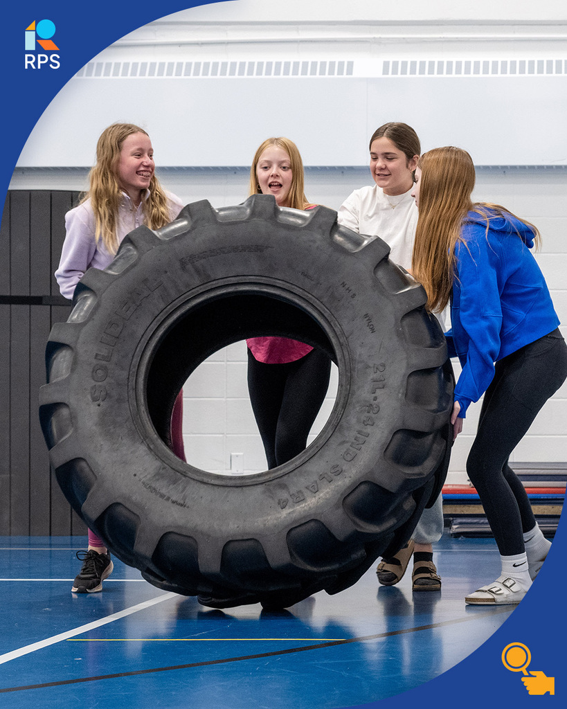 Four middle school girls lift a tractor tire together.