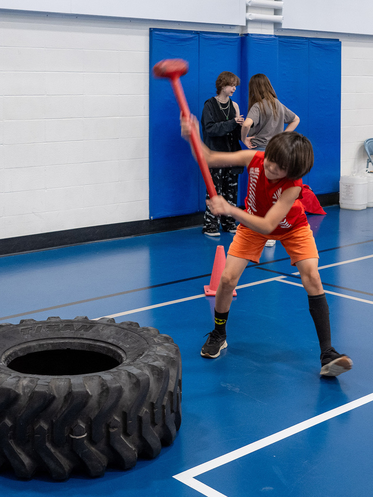 A middle schooler swings a mallet at a tire with gusto!