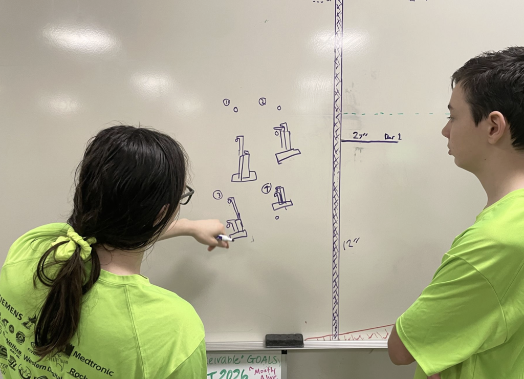 Two robotics team members collaborating on their prototypes on the whiteboard.