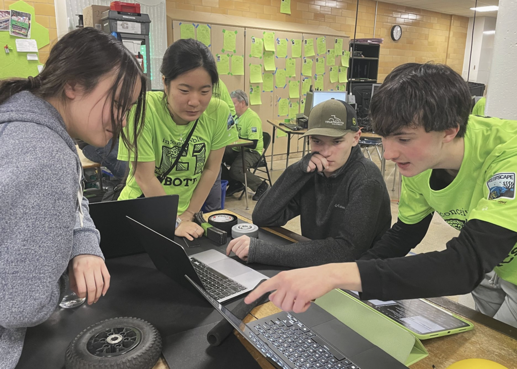 Robotics team members discussing item on computer screen while one member points to screen.