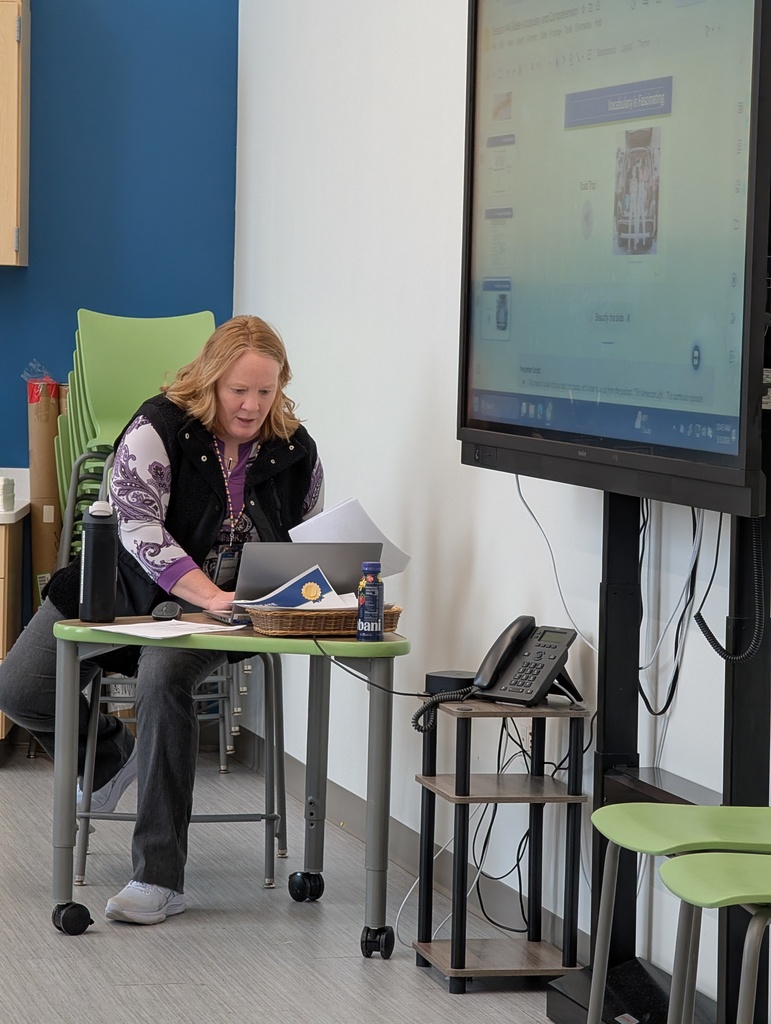 A woman leans over a laptop and her presentation is displayed on a Smartboard.
