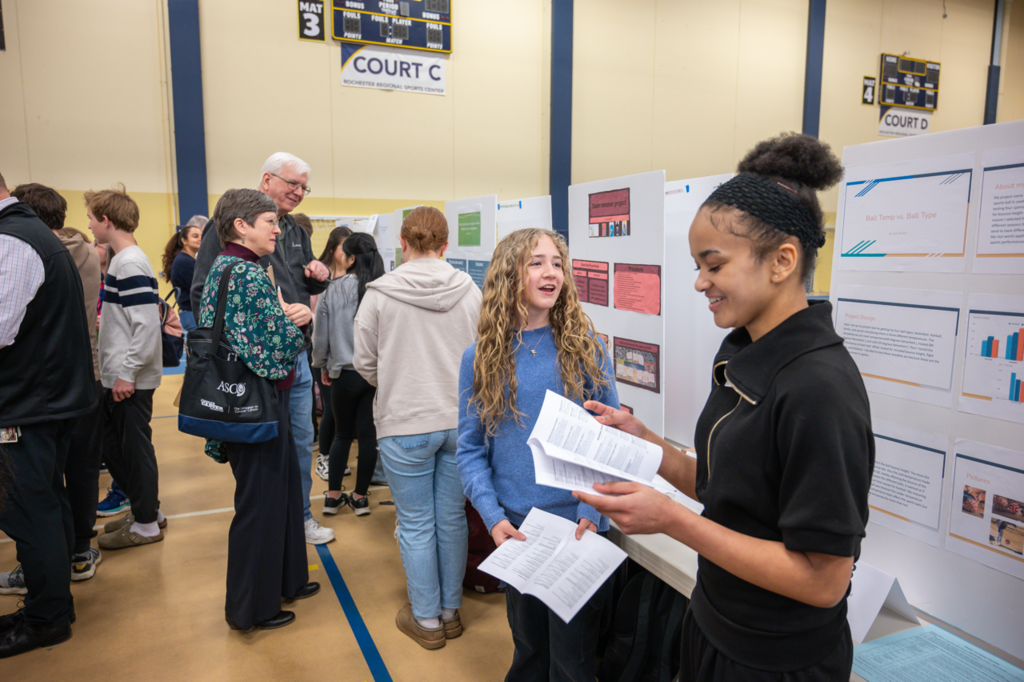 Two students talking together in front of their STEM Fair project boards looking at each other and their program.