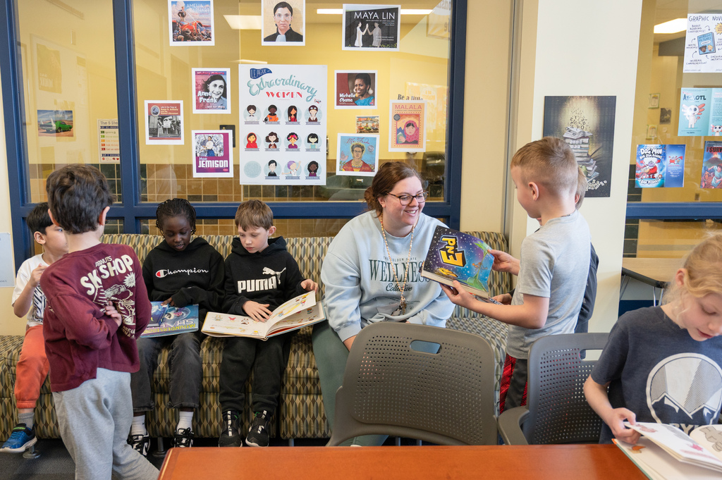 Student talking to the staff member about their book while also sitting next to to other students reading.