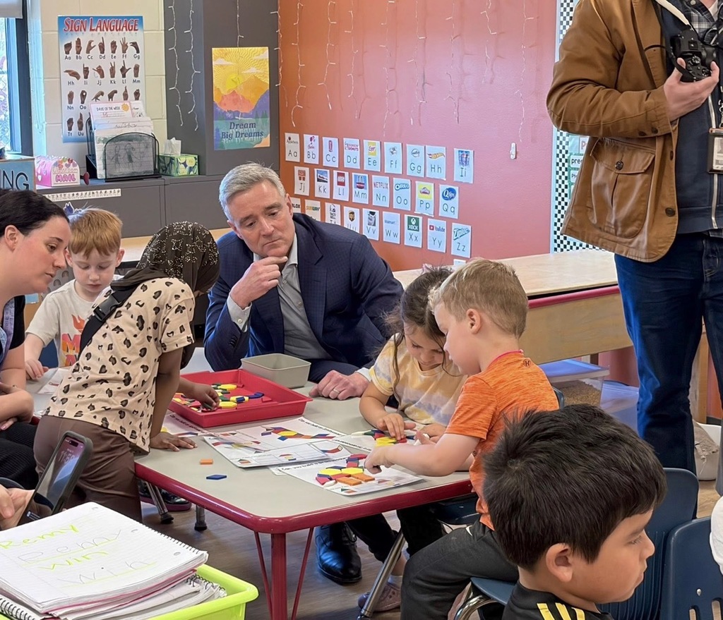 Preschool students working at a table building dinosaurs with parallelogram building blocks as Superintendent Pekel asks them questions about what they are building.