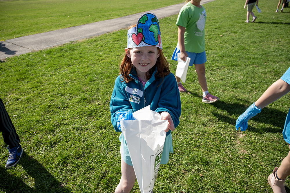Student showing her trashbag with a paper hat she made worn on her head