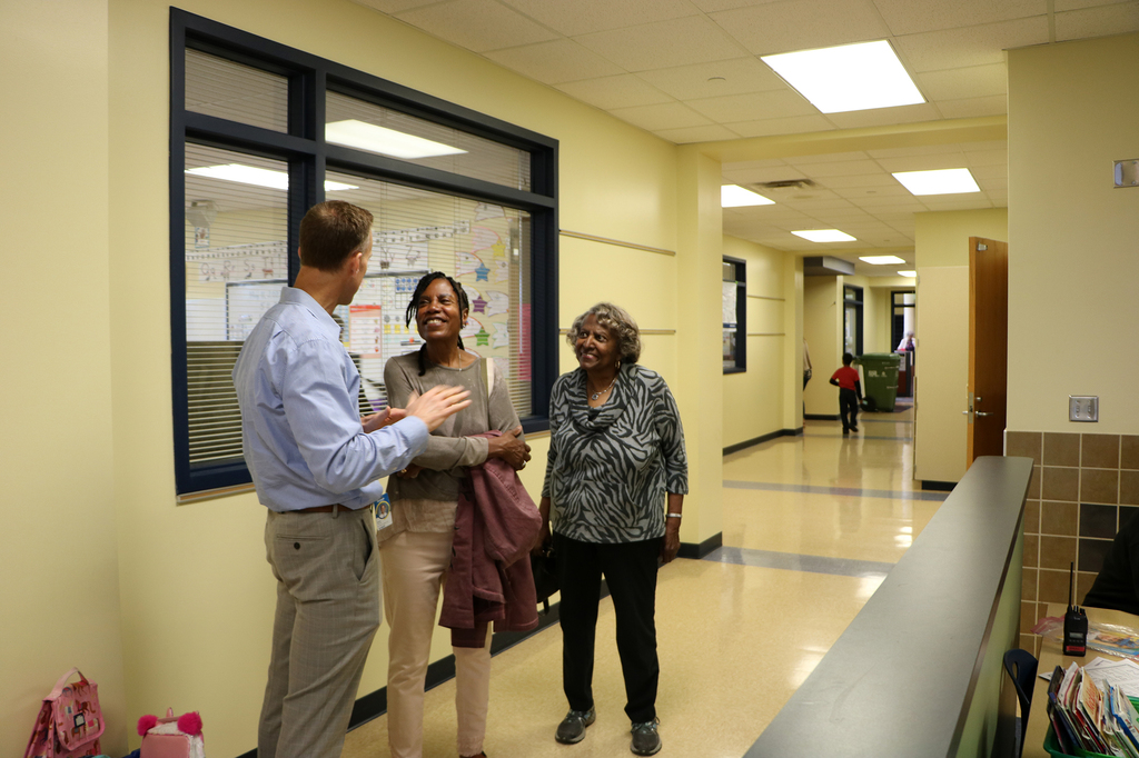 Principal Mark Randall talking with Leilani and Joyce in the school hallway as they look up smiling at him.