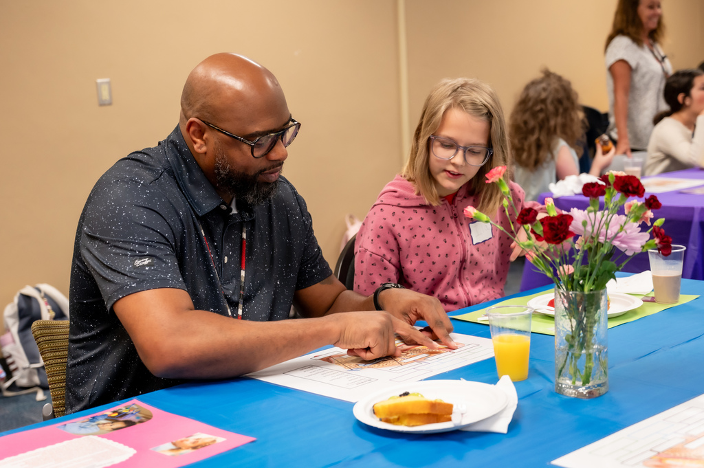 A young student quizzes an athletic director on the parts of the ear at a breakfast event.