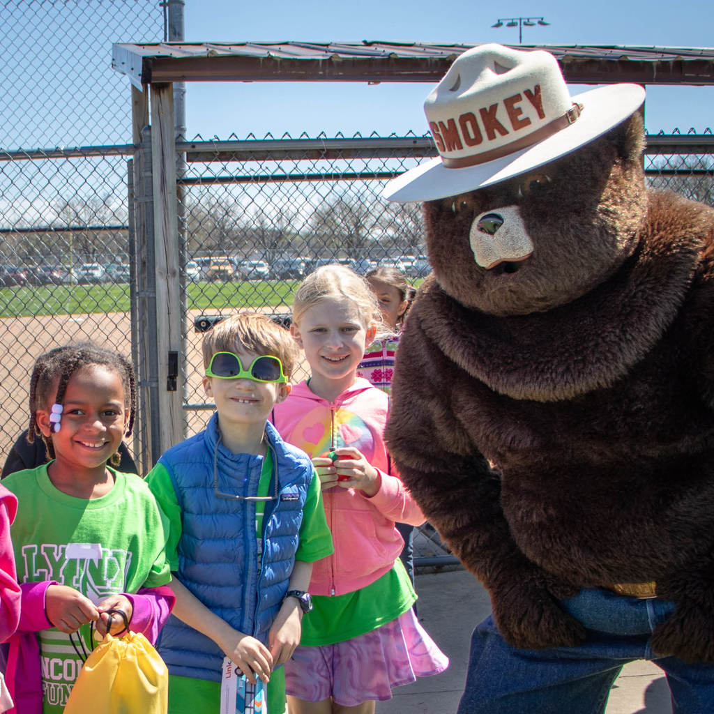 Three students and Smokey the BEar smile at the camera on a sunny day.