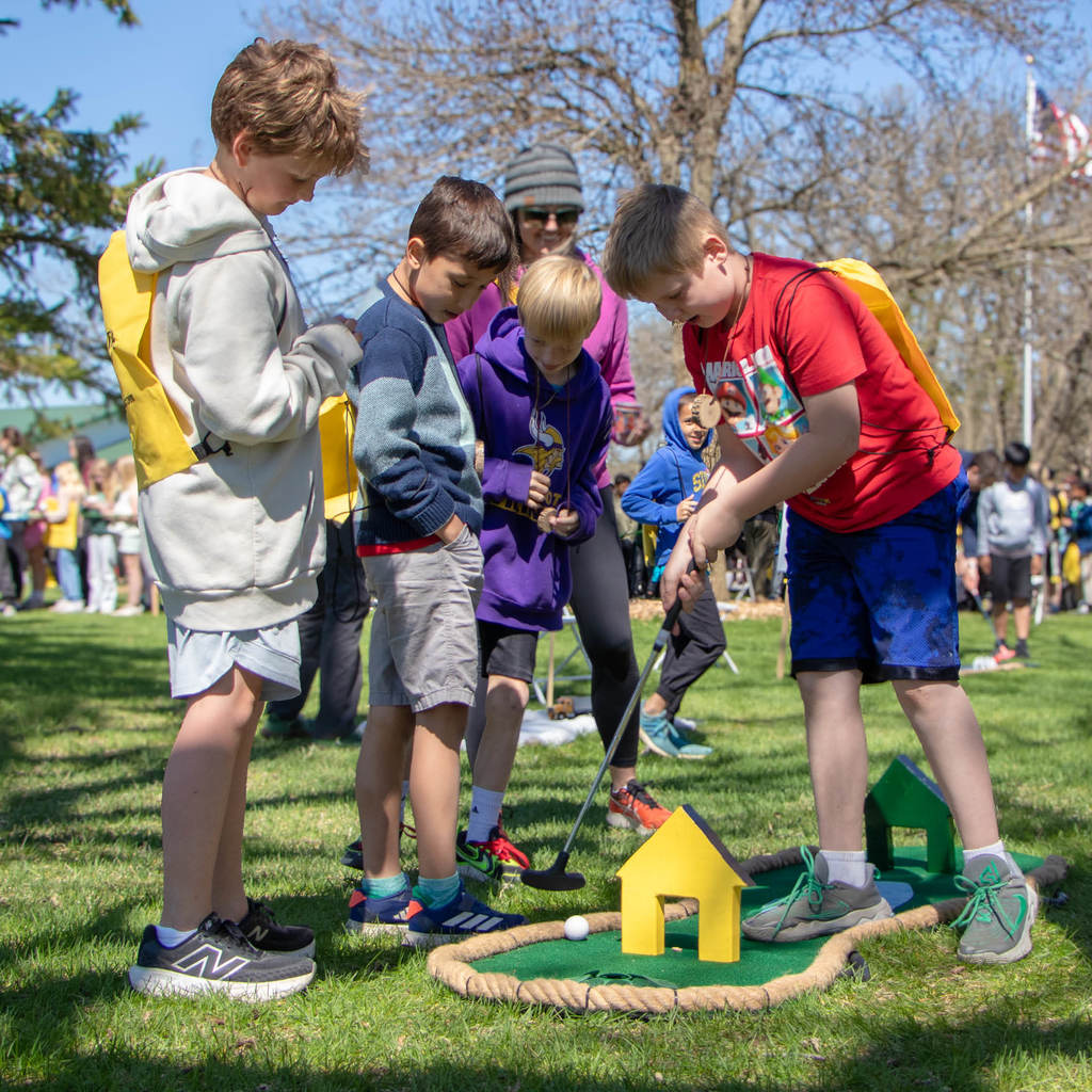 Four boys play put-put goal in the park.