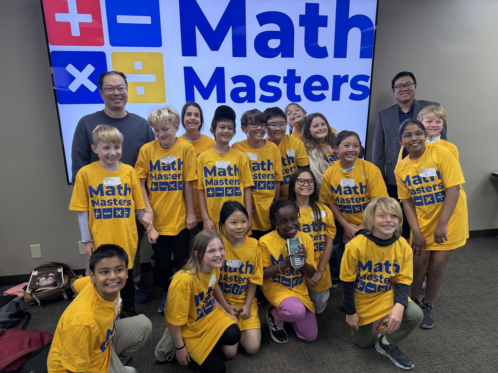 17 Math Masters with two of their teachers posing for a photo in their Math Masters shirts in front of the Math Masters sign.