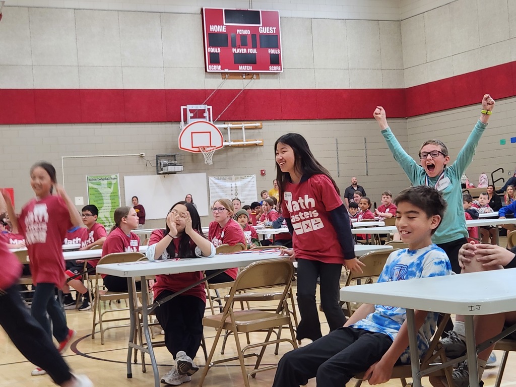 Washington students jumping up to celebrate their win in the middle of the auditorium at Austin Intermediate School.