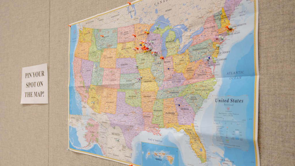 A map of the USA with pins in it hung on a wall. A sign is next to it that says, "Pin your spot of the map!"