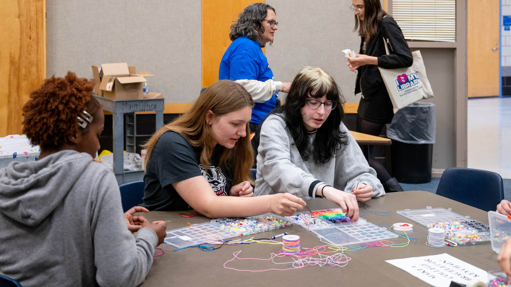 Three seniors sit at a table making beaded bracelets in their chosen college colors.