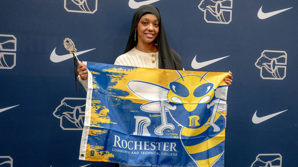 In front of a Century High School backdrop, a senior holds up a colorful RCTC banner.