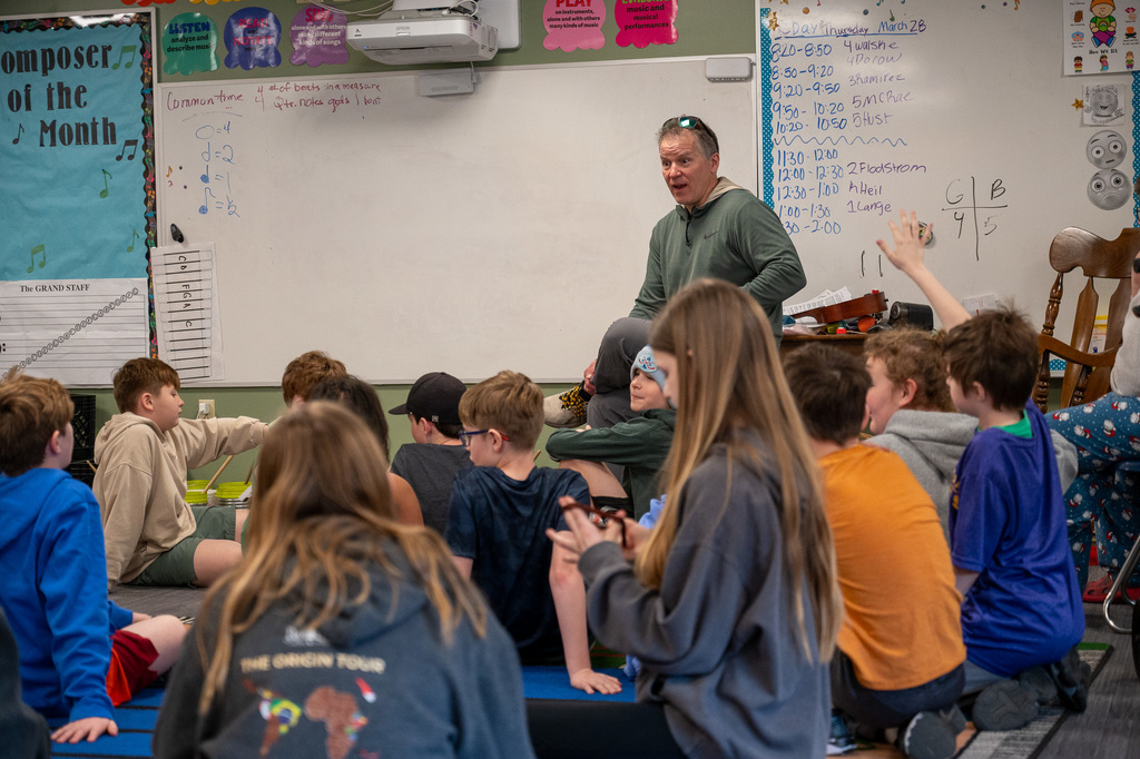Older male teacher standing in front of the whiteboard enthusiastically talking to his students.