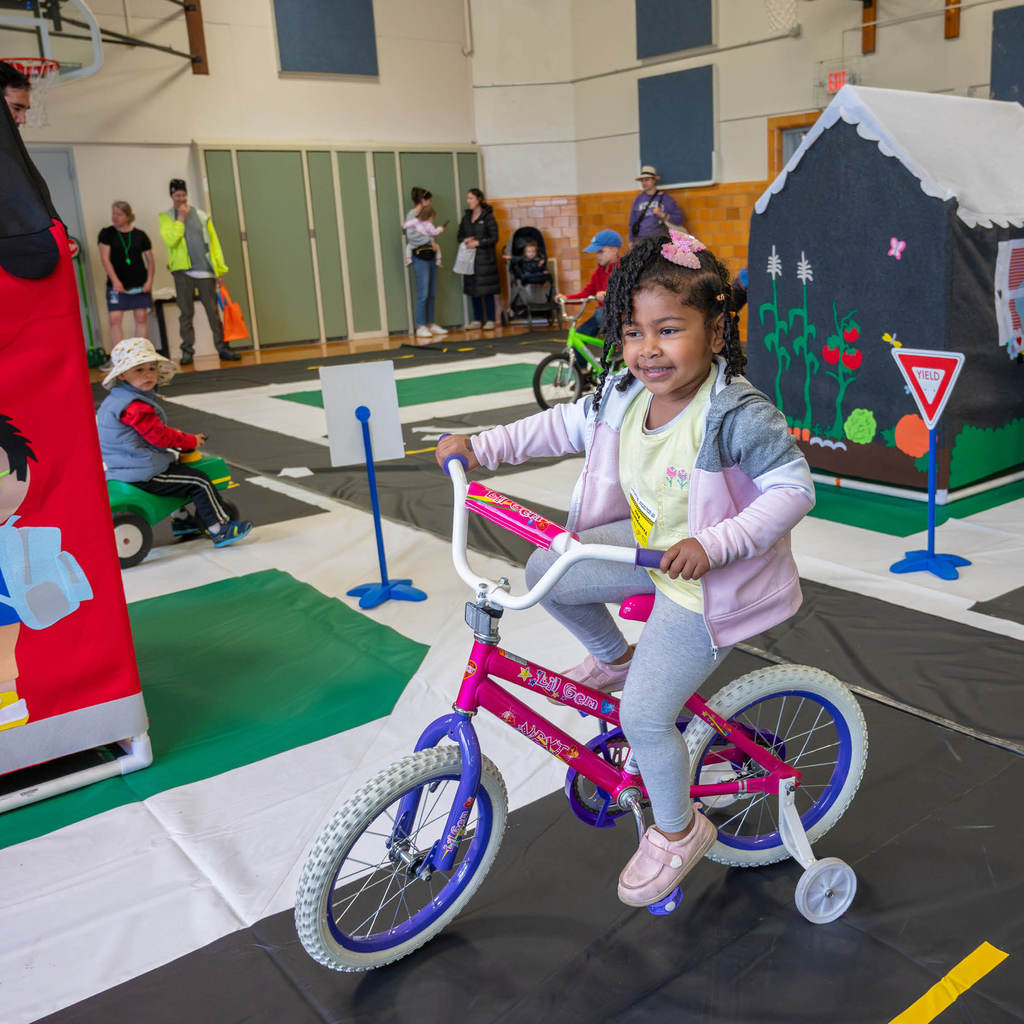 A young girl rides a junior-sized bike on an indoor traffic garden.