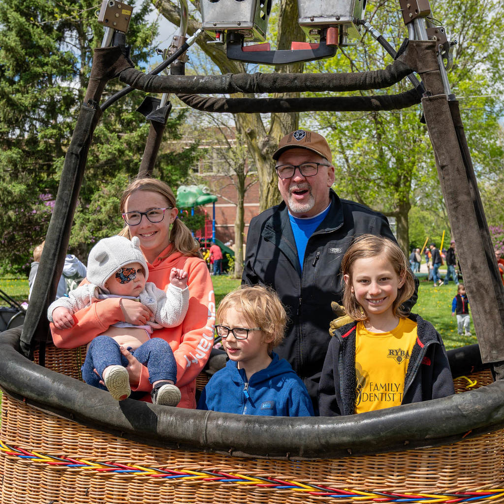 Four siblings smile for the camera in a hot air balloon basket on a sunny day.