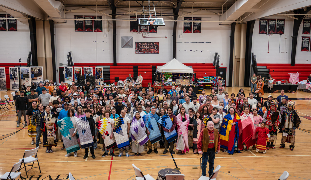 AIE Seniors, AIPAC, and powwow participants all posing for a photo in the center of the John Marshall gym.