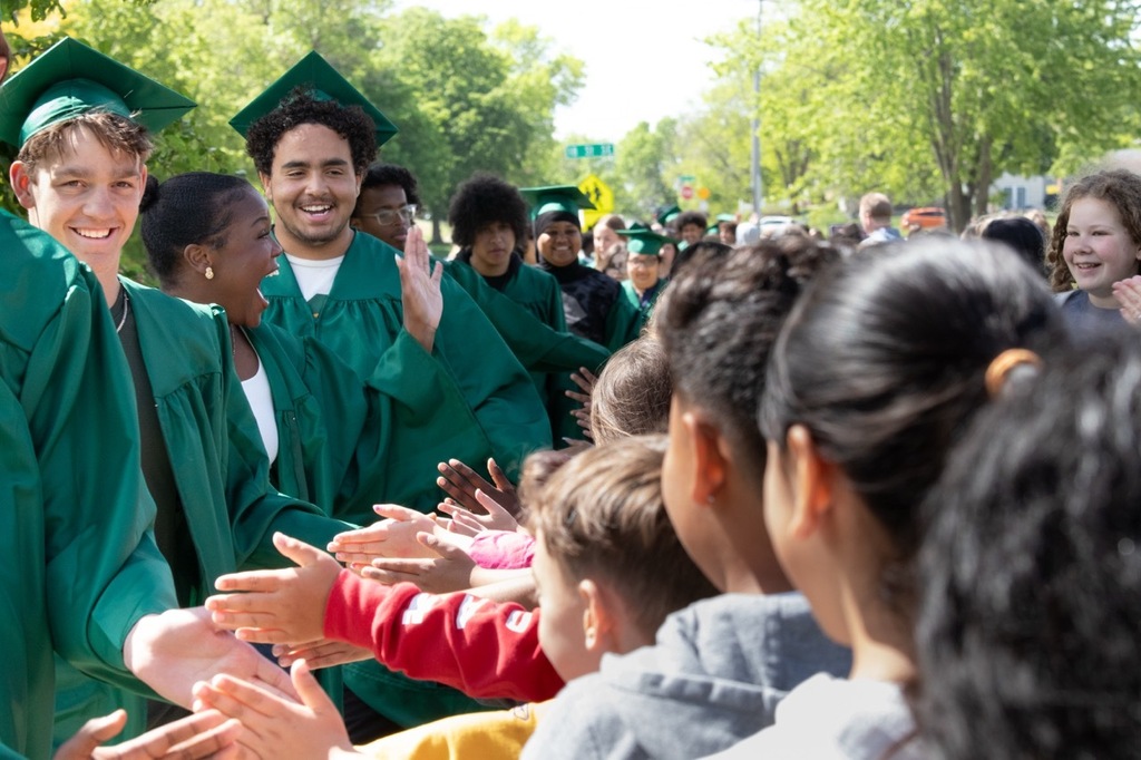 Mayo seniors in cap and gown walking outside of Franklin Elementary high-fiving elementary students that are lined up on the sidewalks.