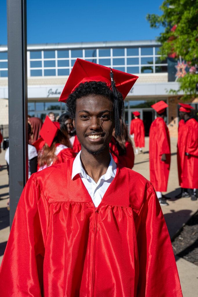 JM Senior standing in front of the school smiling for the photo in cap and gown.
