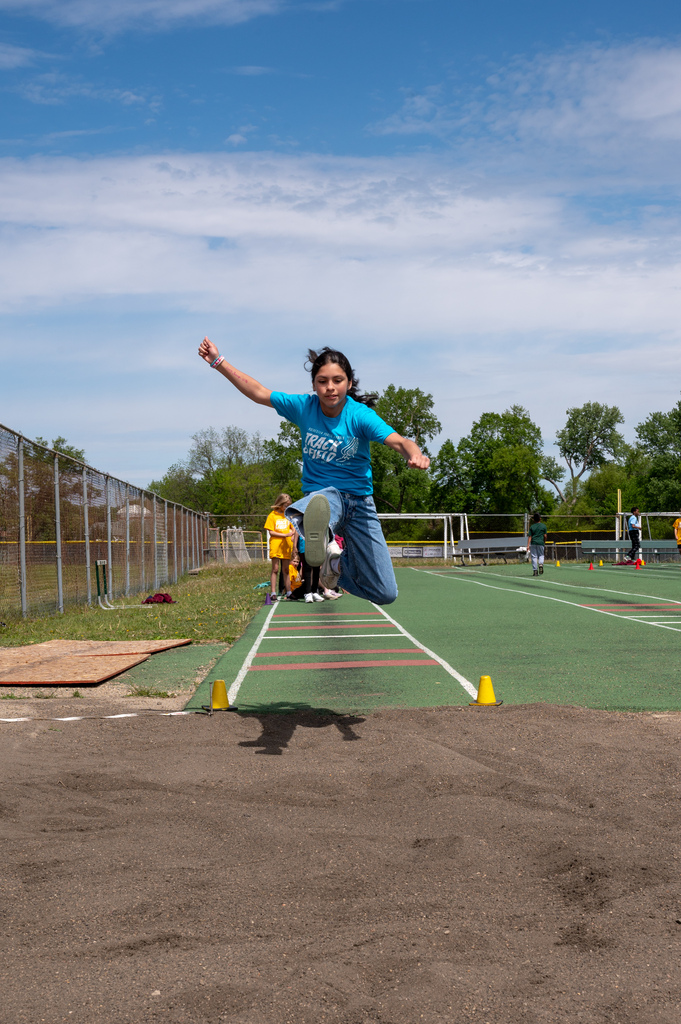 Student mid-air as they prepare to land in the sand of the long jump.