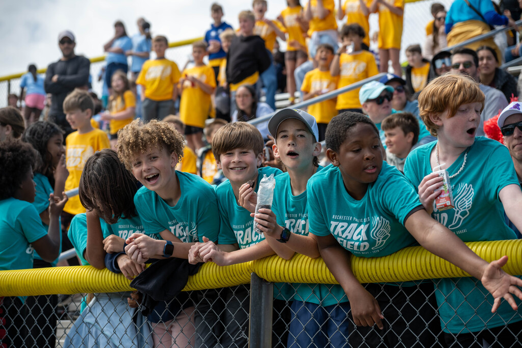Students cheering on friends, eating snacks, and smiling at the camera from the bleachers.