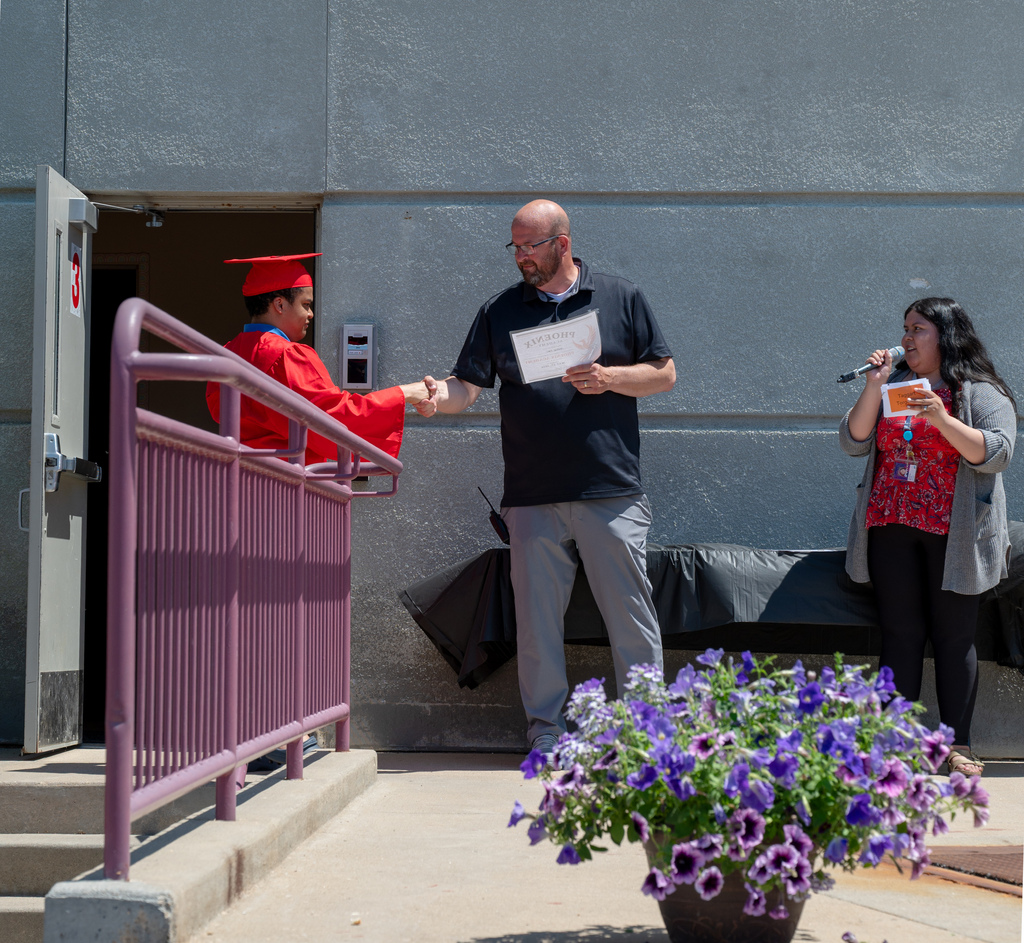On stage outside, a graduate holds shakes his principal's hand before receiving his diploma