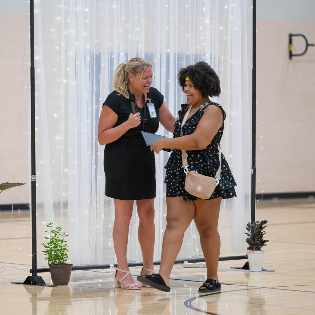 A principal and graduate laugh as the grad receives her diploma.