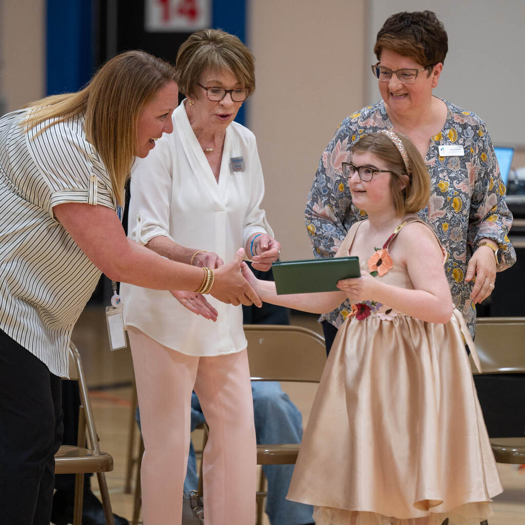 A graduate in a satin dress holds her diploma and shakes the hand of a staff member.