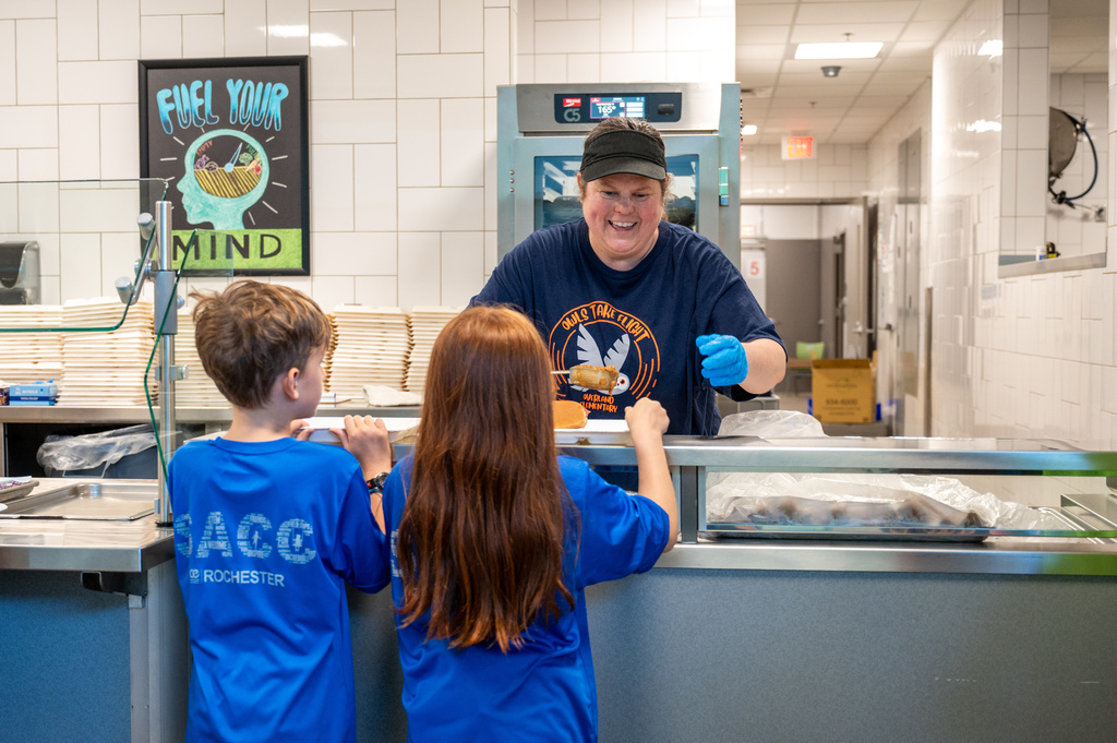 SNS worker at Overland elementary school serving students lunch to two students in SACC shirts.