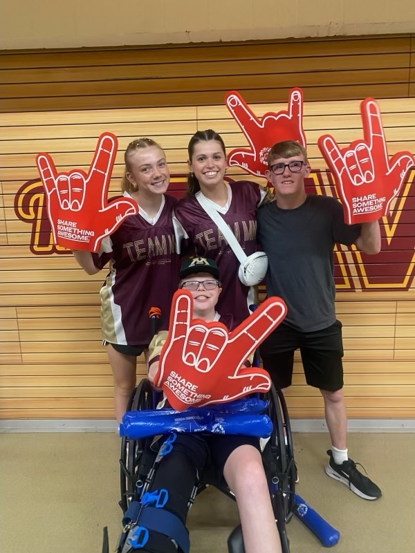 Students holding foam fingers that state "share something awesome" celebrating at the special olympics.