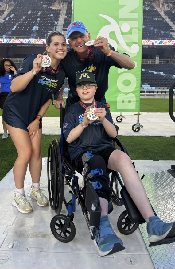 Two Rochester students posing with an olympian for a photo with medals at the Special Olympics.