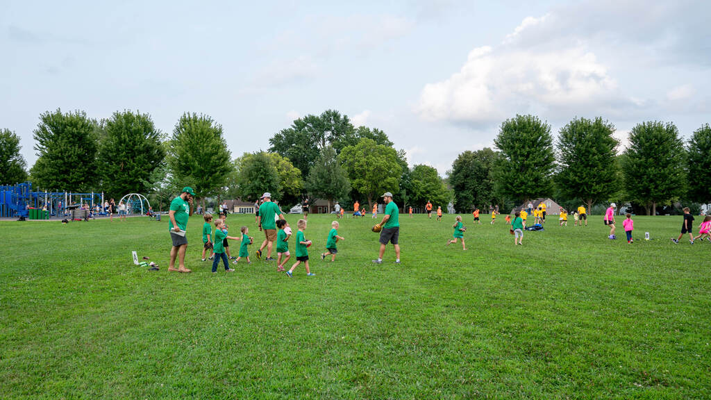 A wideshot of tball teams in matching bright shirts grouping up to practice.