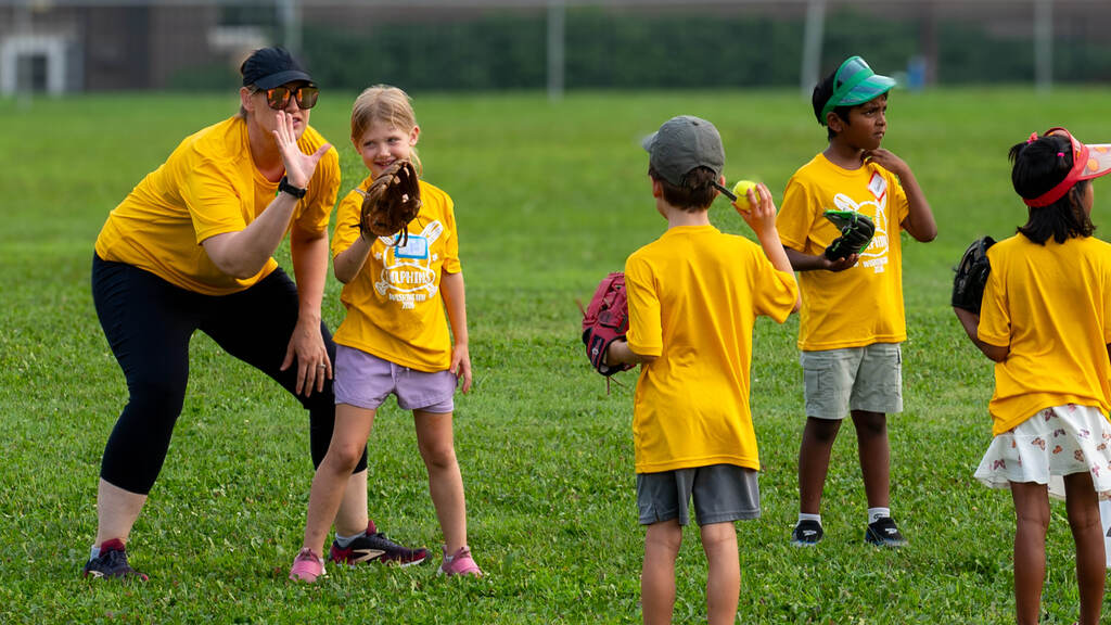 A coach demonstrates how to hold a baseball mitt for the kids practicing throwing to one another.